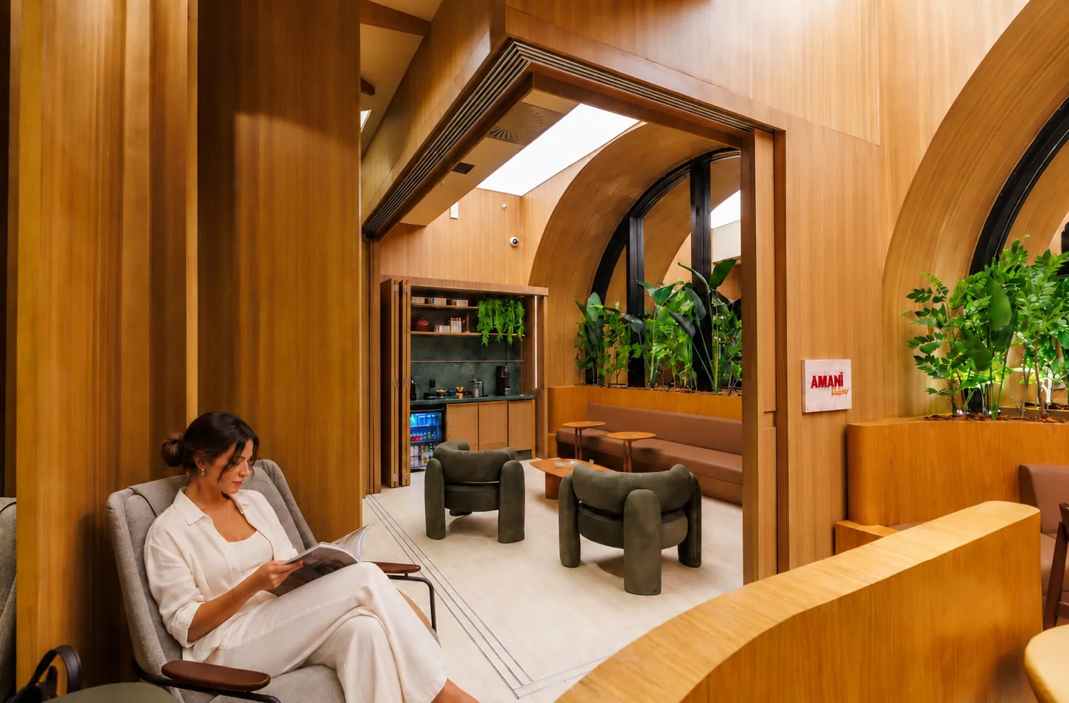 Pasajera leyendo una revista en un sillón gris, con sillones verdes y plantas en la sala al fondo