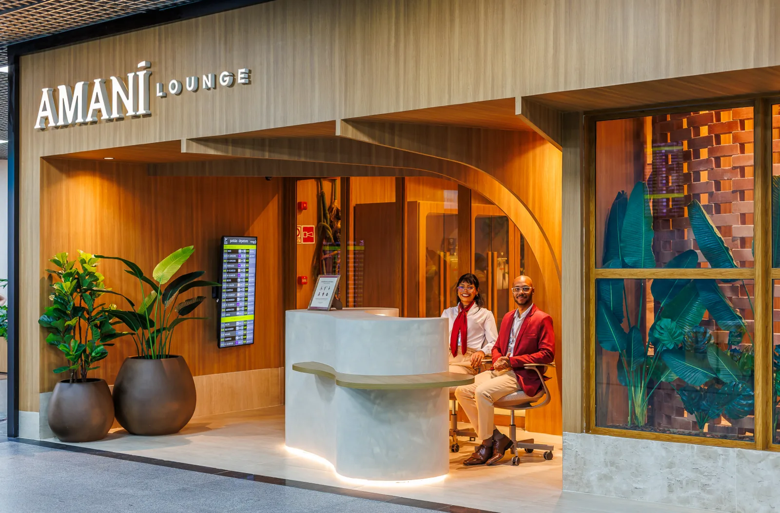 Entrada del Amaní Lounge, con fachada de madera y dos recepcionistas de uniforme rojo sentados en el mostrador de recepción